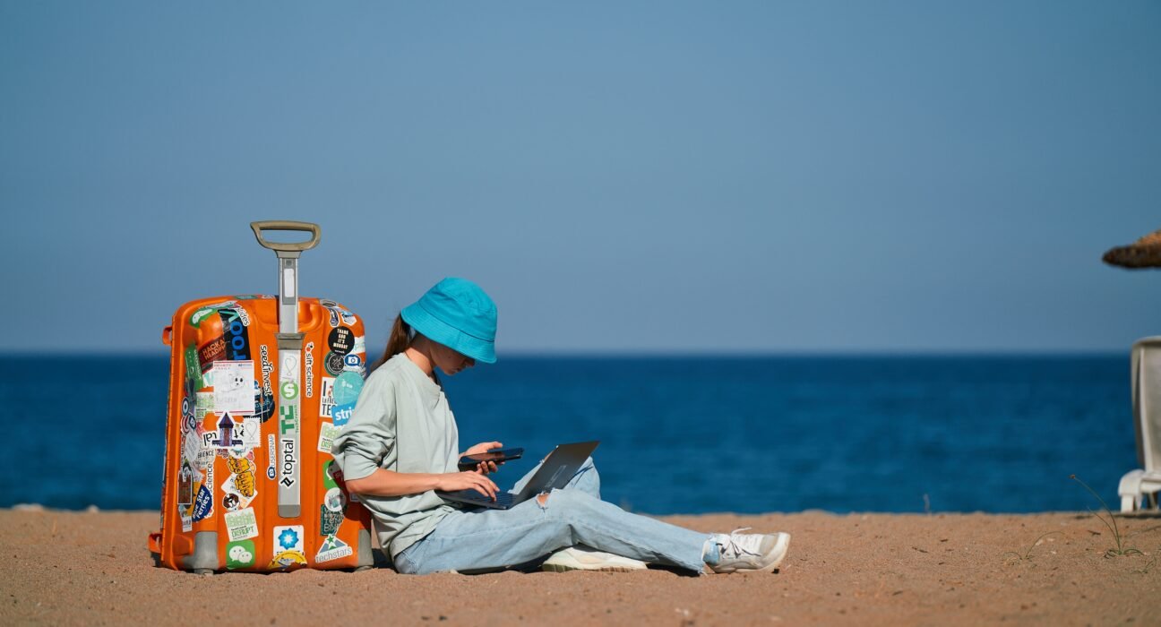 girl remote worker sits on the beach with a suitcase and works while on vacation