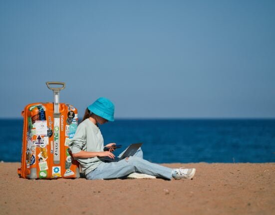 girl remote worker sits on the beach with a suitcase and works while on vacation