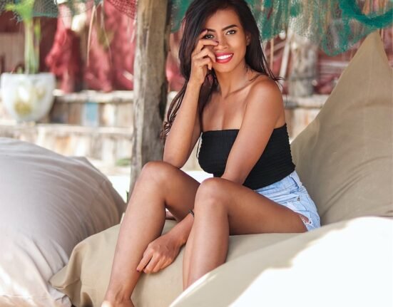 woman in black brassiere and blue shorts sitting on white bed