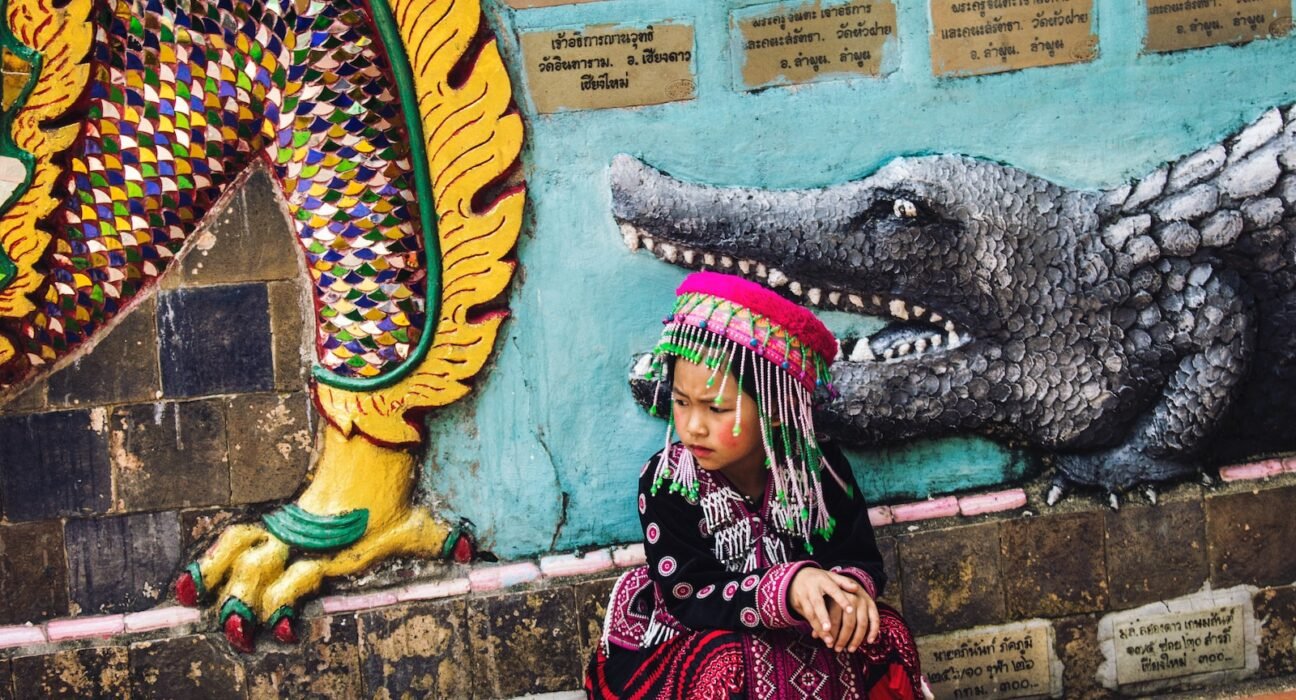 girl wearing multicolored traditional dress sitting near the wall