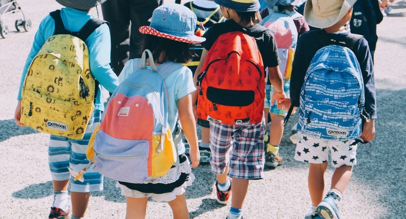 group of people wearing white and orange backpacks walking on gray concrete pavement during daytime