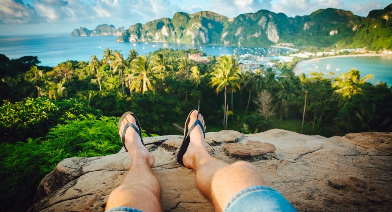 person wearing black flip-flops sitting on rock