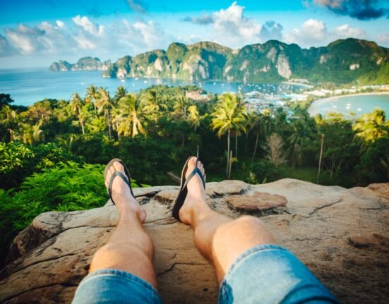 person wearing black flip-flops sitting on rock