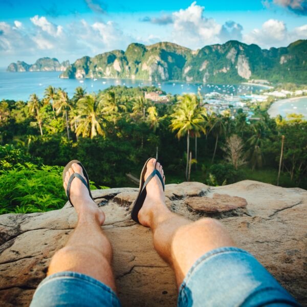 person wearing black flip-flops sitting on rock