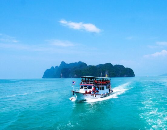 boat with peoples sailing on body of water with island background