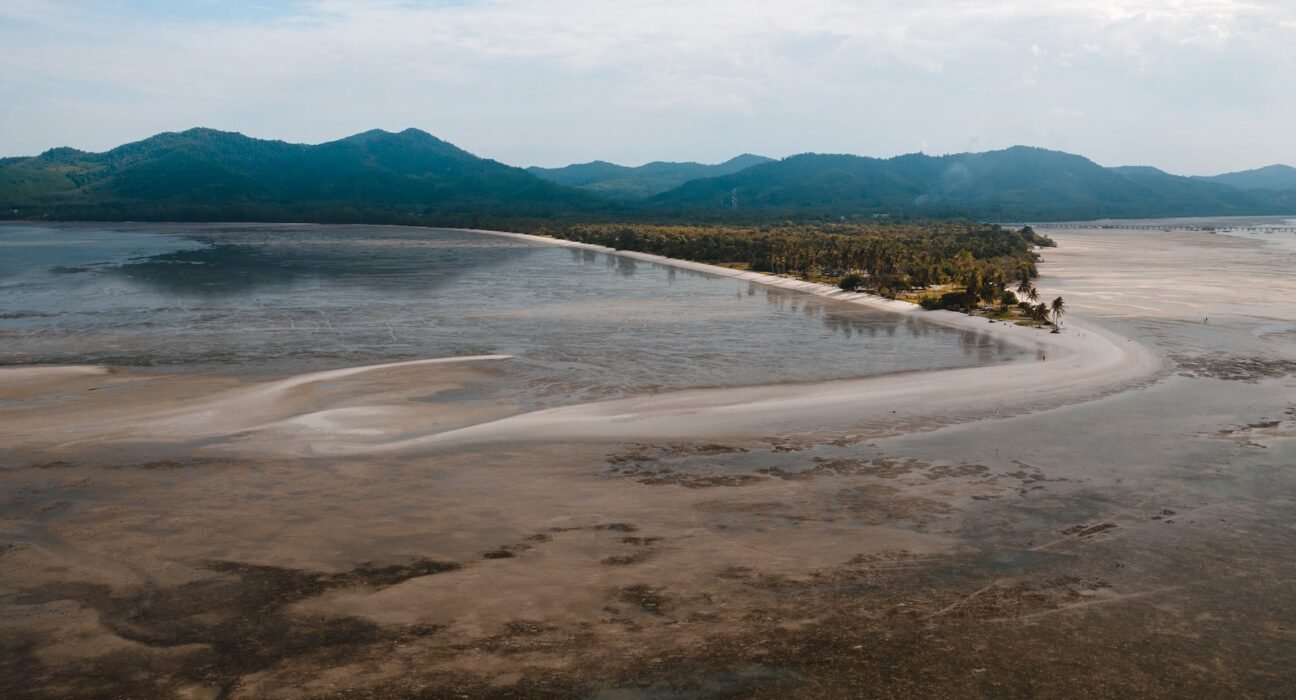 body of water near mountain under white clouds during daytime