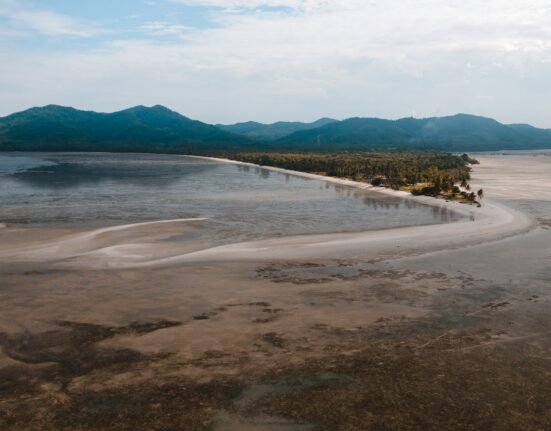 body of water near mountain under white clouds during daytime
