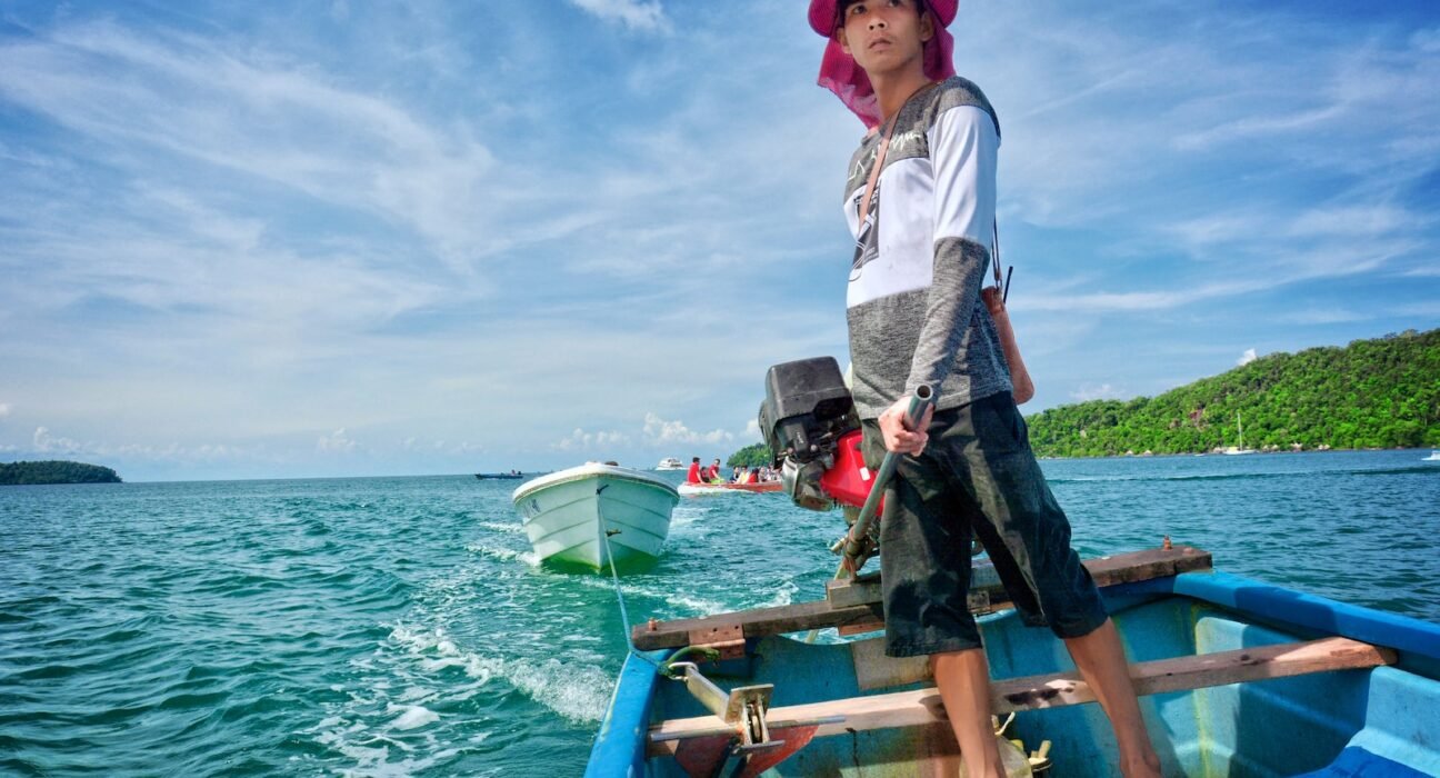man in white dress shirt and black pants sitting on brown wooden boat during daytime