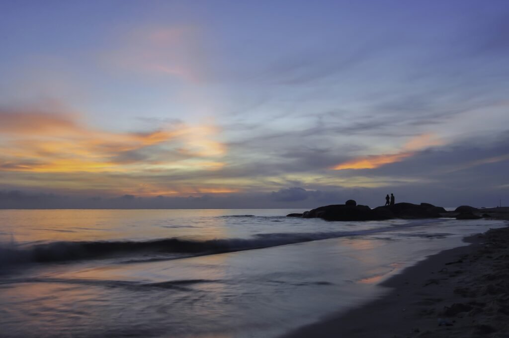 two people standing on rocks in the ocean to watch the sunrise.
