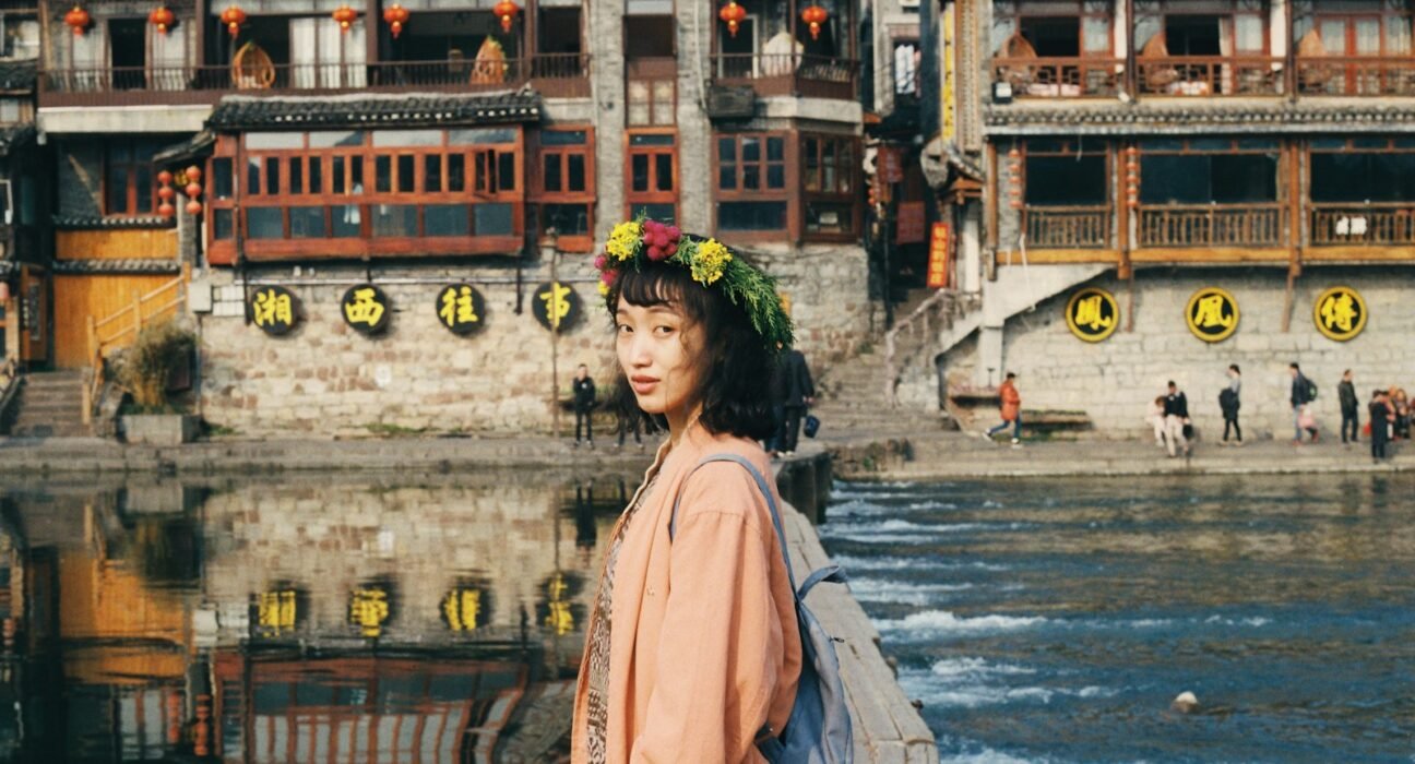 woman in pink dress standing in front of lake near temples