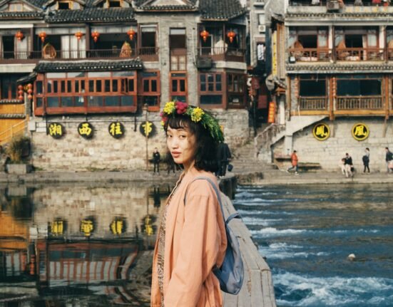 woman in pink dress standing in front of lake near temples