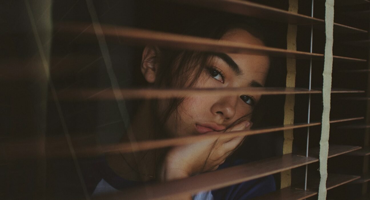 a woman looking out of a window with blinds