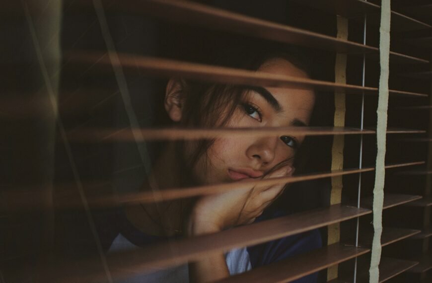 a woman looking out of a window with blinds