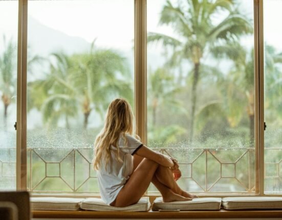 woman sitting on white cushion near glass window