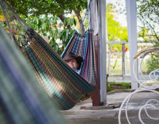 man laying down on multicolored hammock hanged on porch column
