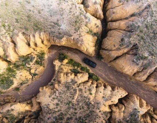 An aerial view of a car driving on a dirt road