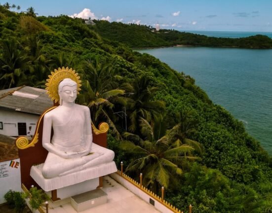 a statue of a person sitting on a bench by a body of water